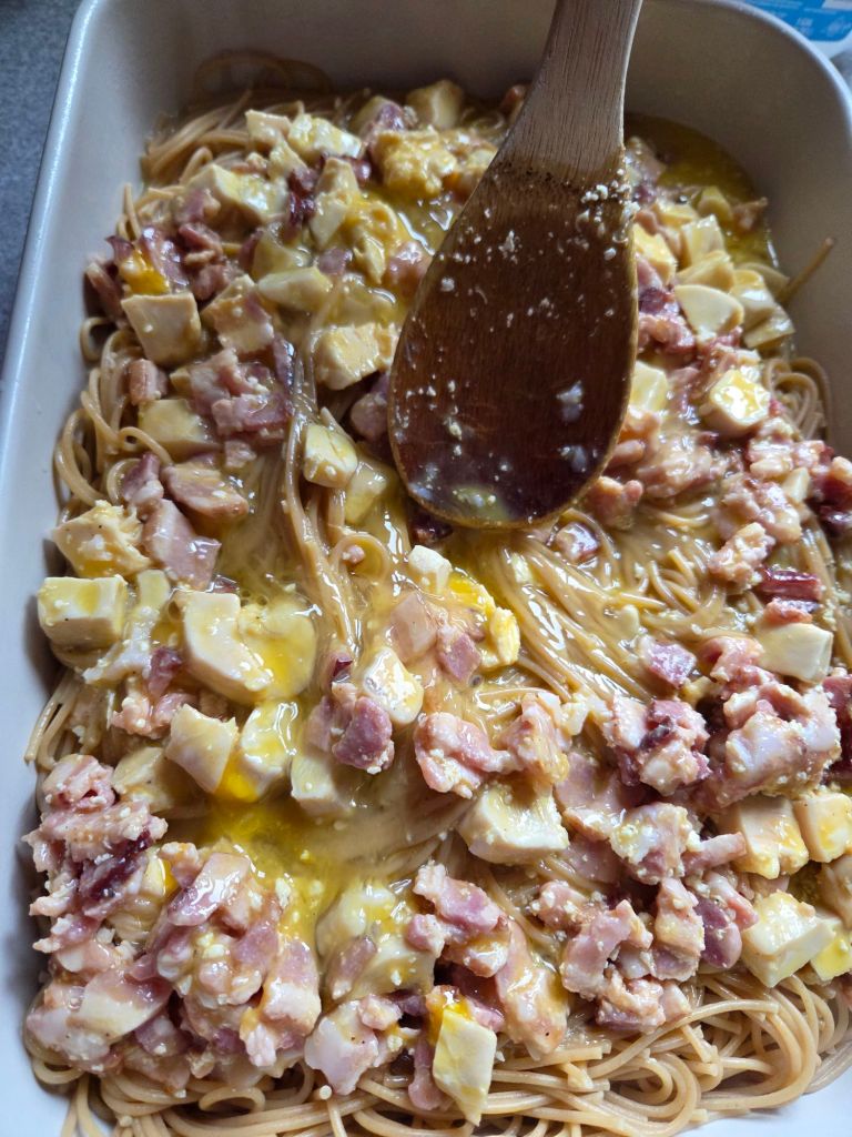 Egg, bacon, chicken mixutre poured over noodles